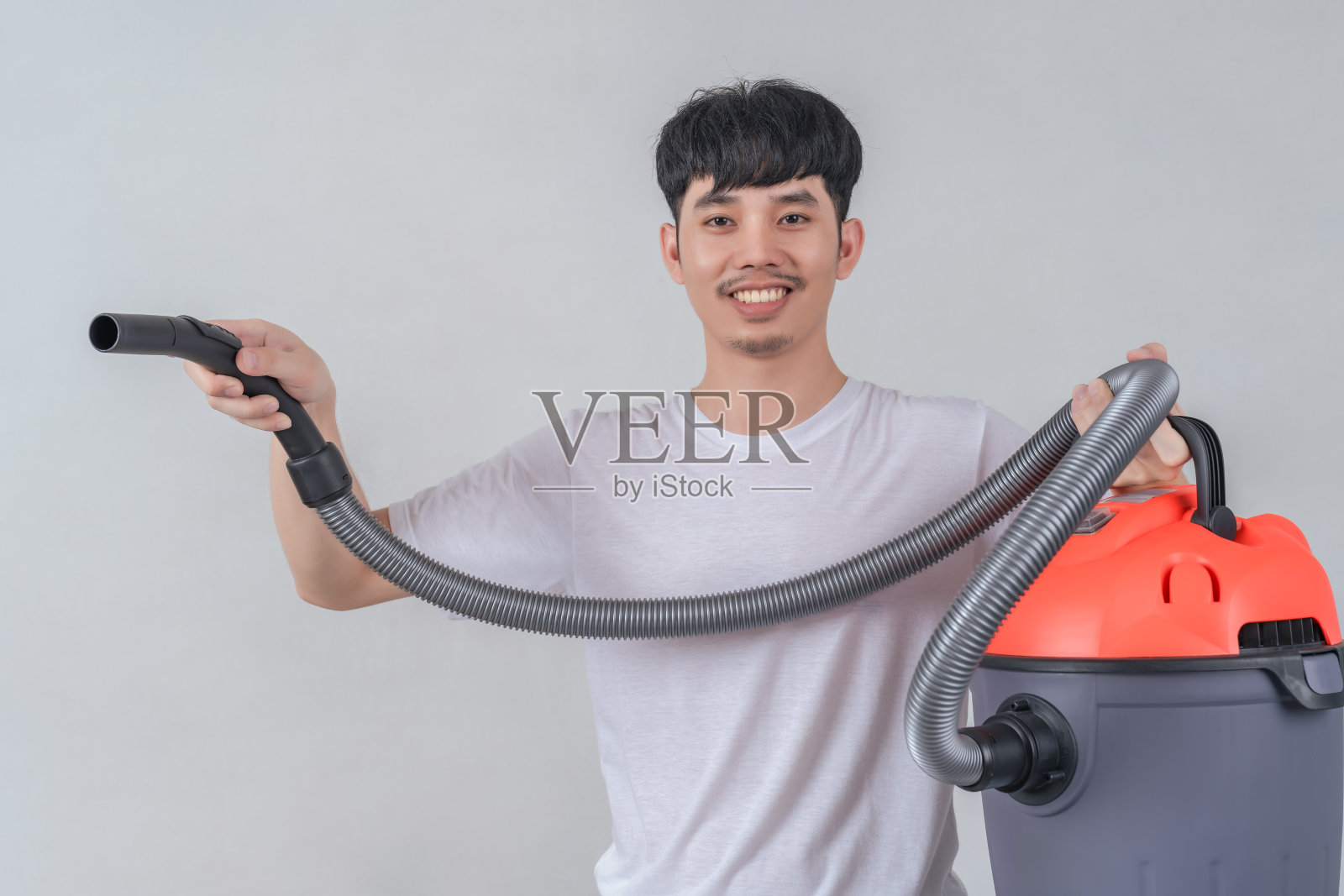 英俊的年轻人拿着吸尘器打扫卫生,开心地笑着。照片摄影图片