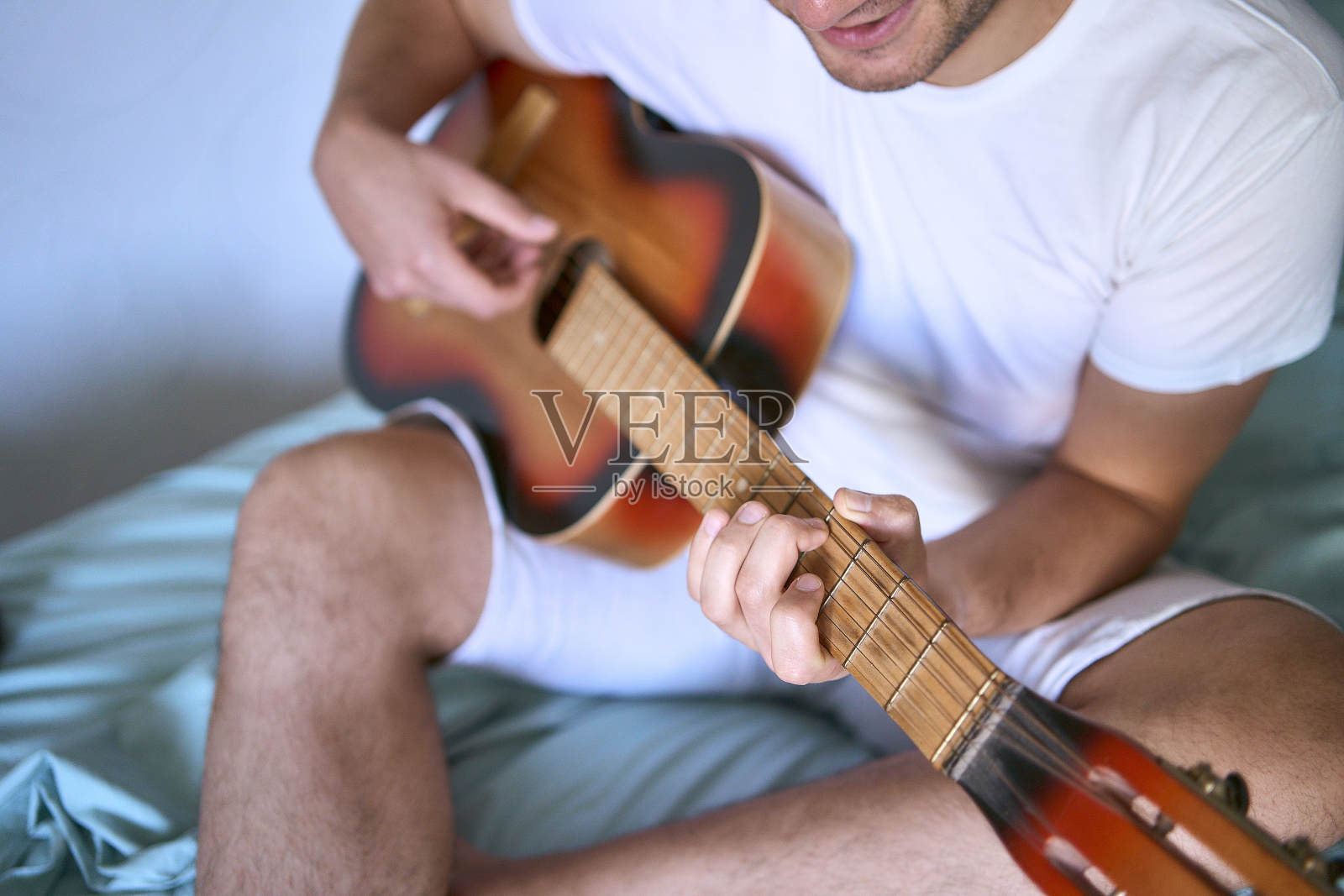 一个年轻人正在家里学弹吉他,一只猫躺在他旁边听着照片摄影图片