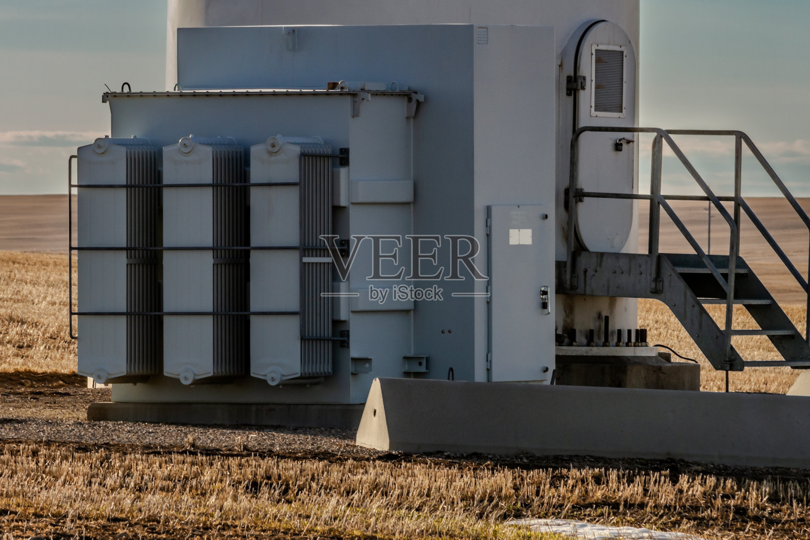 风力发电机底座,有变压器箱、门、栏杆和楼梯,映衬着昏暗的天空照片摄影图片