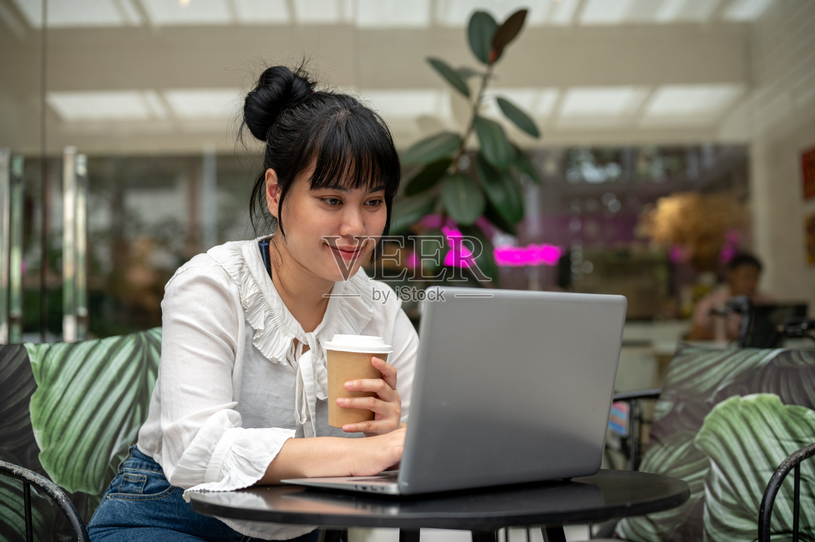 一位年轻的亚洲女性正在咖啡店远程办公,一边喝着咖啡,一边用笔记本电脑工作照片摄影图片