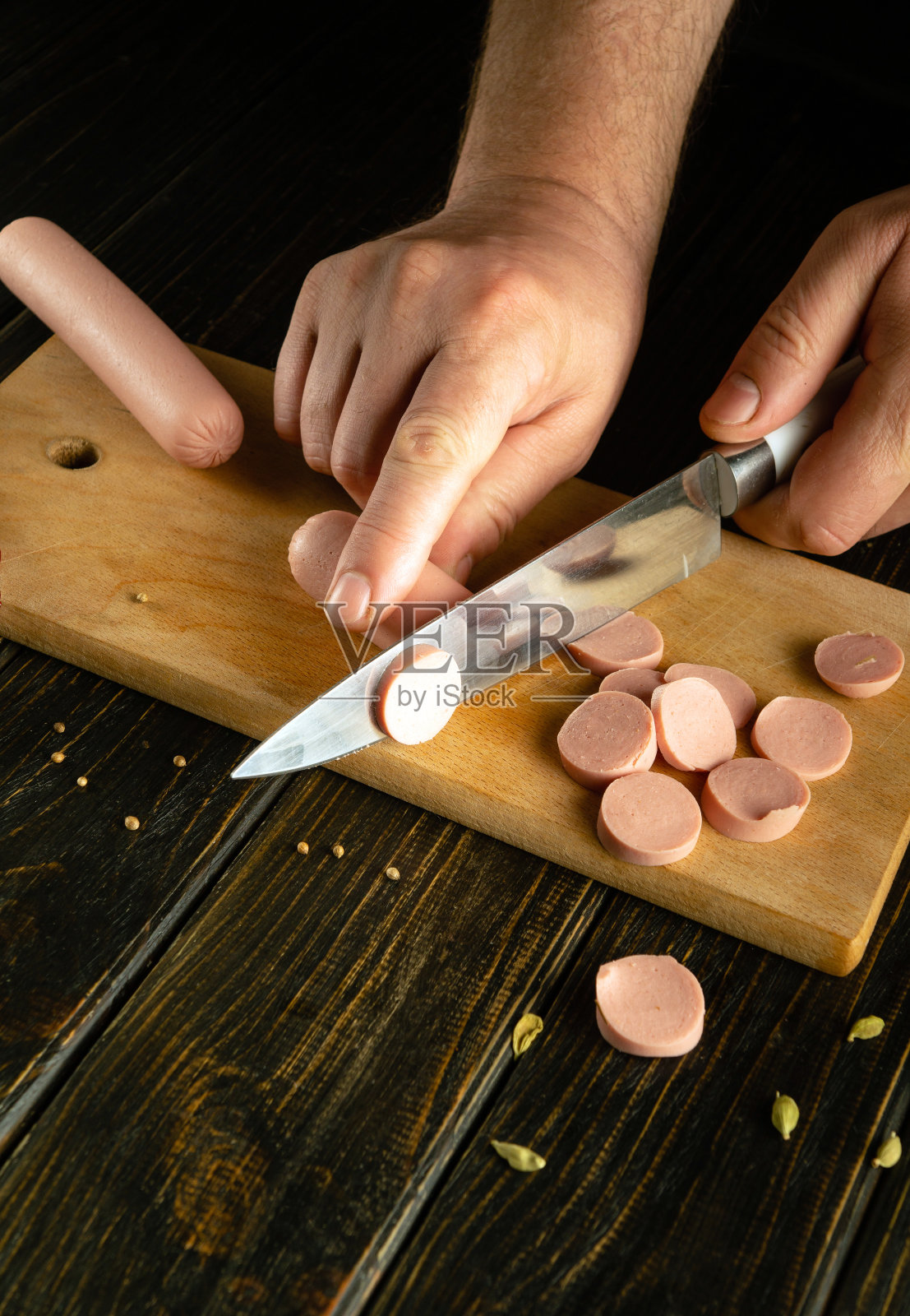 厨师用刀在切菜板上切维也纳香肠,准备午餐。黑色背景上的广告空间照片摄影图片