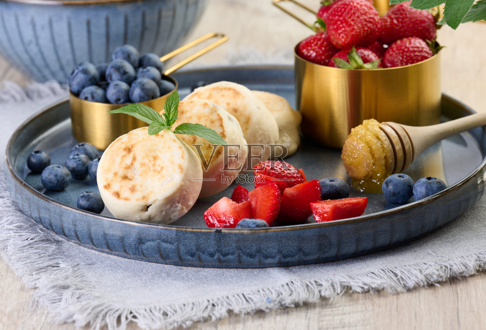 蓝色盘子里放着圆形的小煎芝士蛋糕和浆果。健康的早餐照片摄影图片