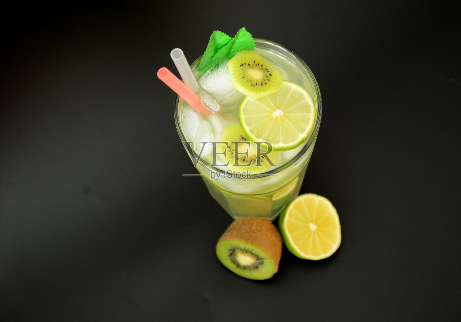 一杯在黑色背景上混合了冰和吸管的果汁,旁边是成熟的猕猴桃和酸橙。照片摄影图片