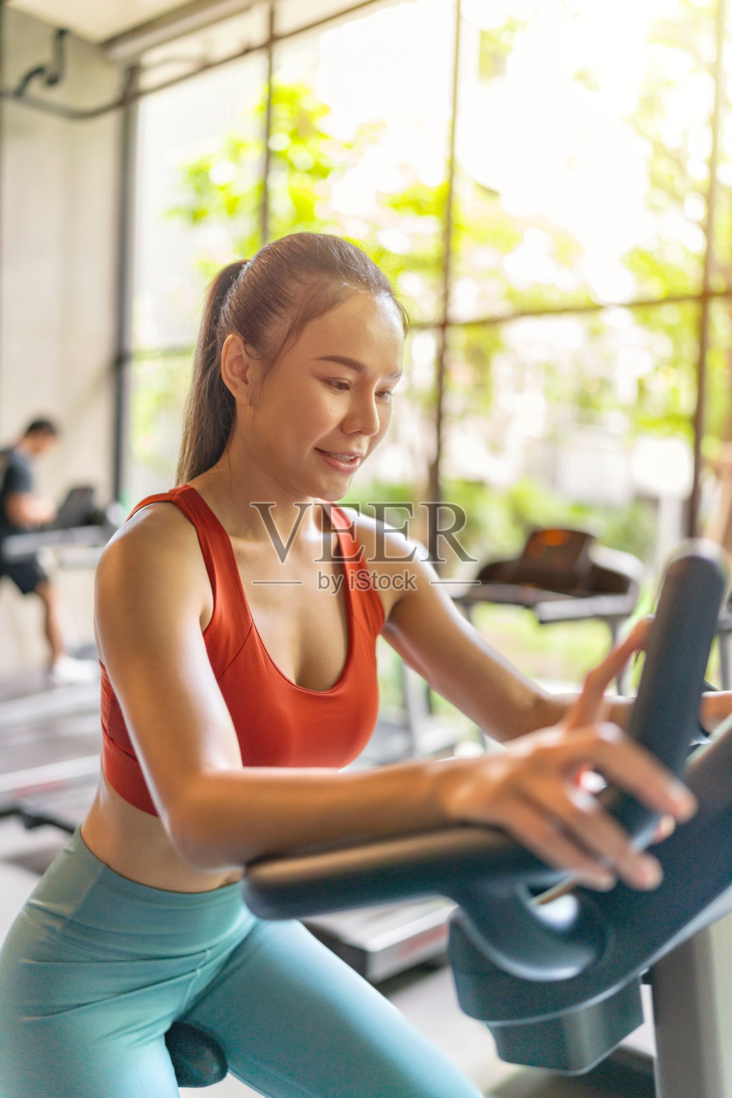 一名亚洲女性在光线充足的健身房里骑着健身车,并拥有花园景观照片摄影图片