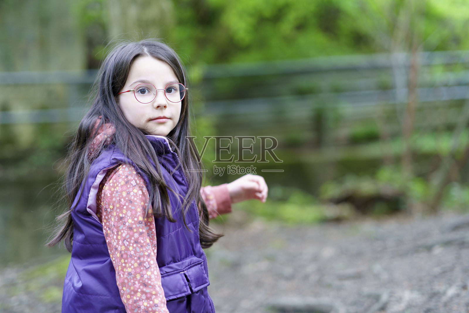一个戴着眼镜、穿着背心的长发小女孩站在森林里照片摄影图片