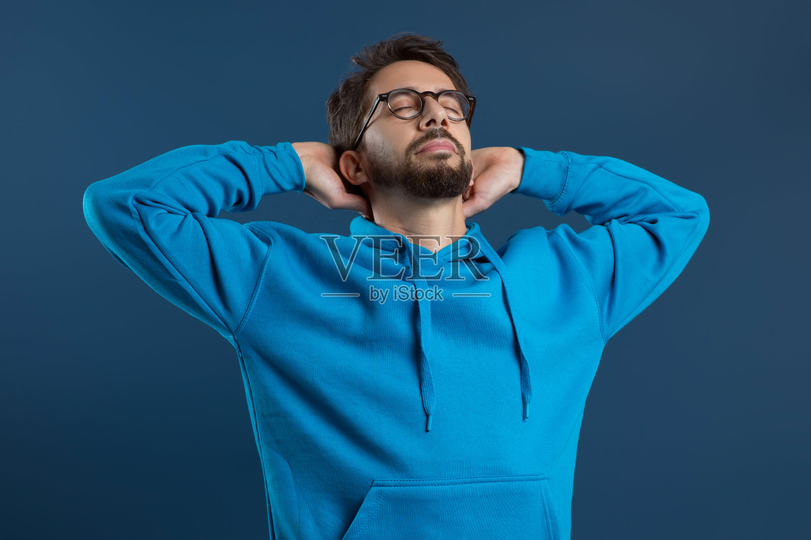 满足的年轻人戴着眼镜,双手放在脑后照片摄影图片