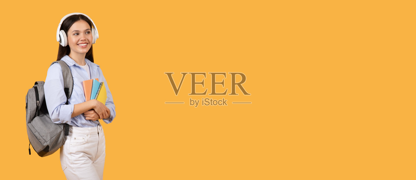 微笑的女学生带着耳机和笔记本寻找空闲空间照片摄影图片