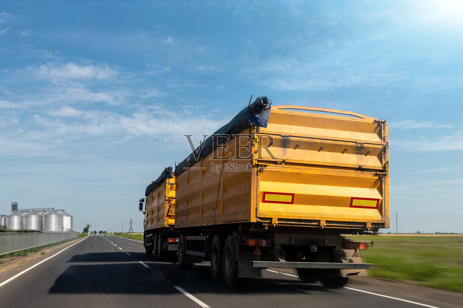 夏日晴空万里,一辆大型现代黄色料斗货车在高速公路上驶往粮仓仓库卸货。谷物收获和运输的工业季节照片摄影图片