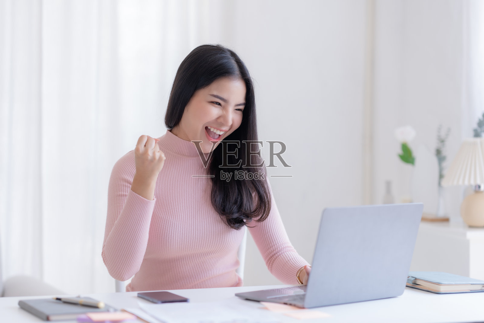 快乐的年轻亚洲女性举起胜利的手,在家里用笔记本电脑开心地微笑。成功,胜利,胜利,胜利,祝贺,概念。照片摄影图片