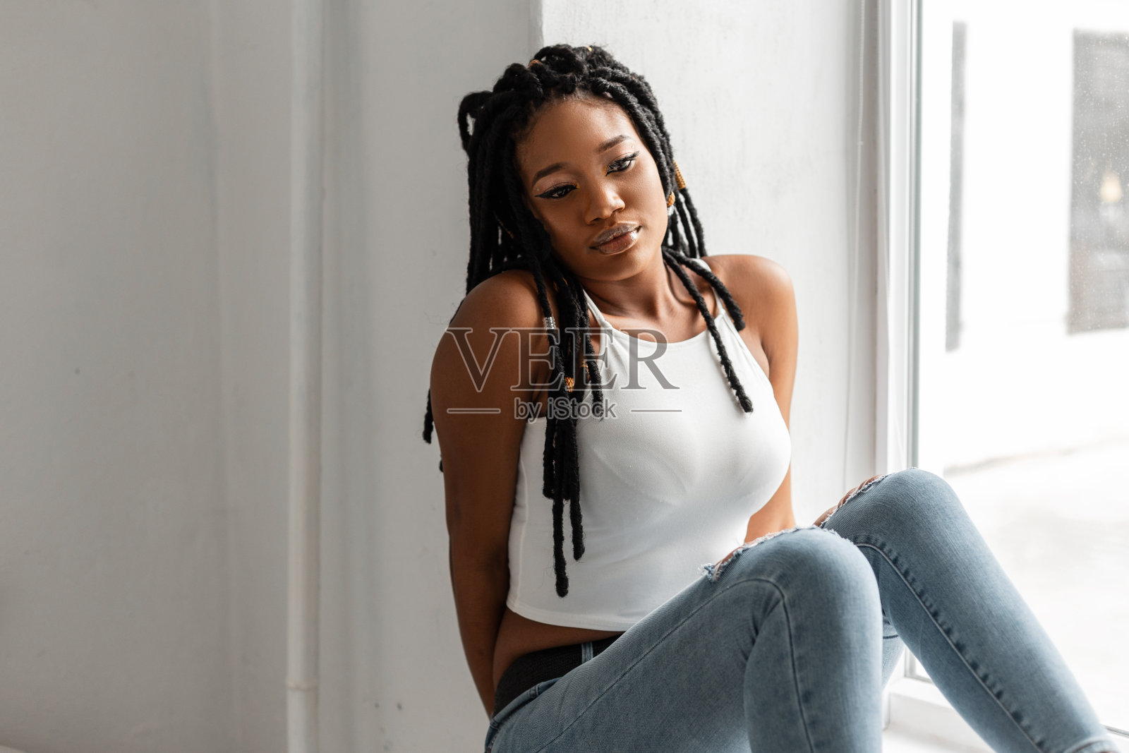 时尚的非洲女人与酷脏辫与白色上衣在时尚的牛仔裤在时尚的牛仔夹克在腰部。美丽的非洲裔美国女人,时尚的发型,在室内复古的衣服照片摄影图片