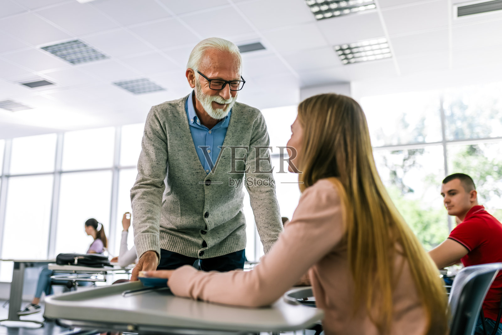 一群学生在上课时拿着书。学生们正在听一位年长的高中老师讲课。照片摄影图片