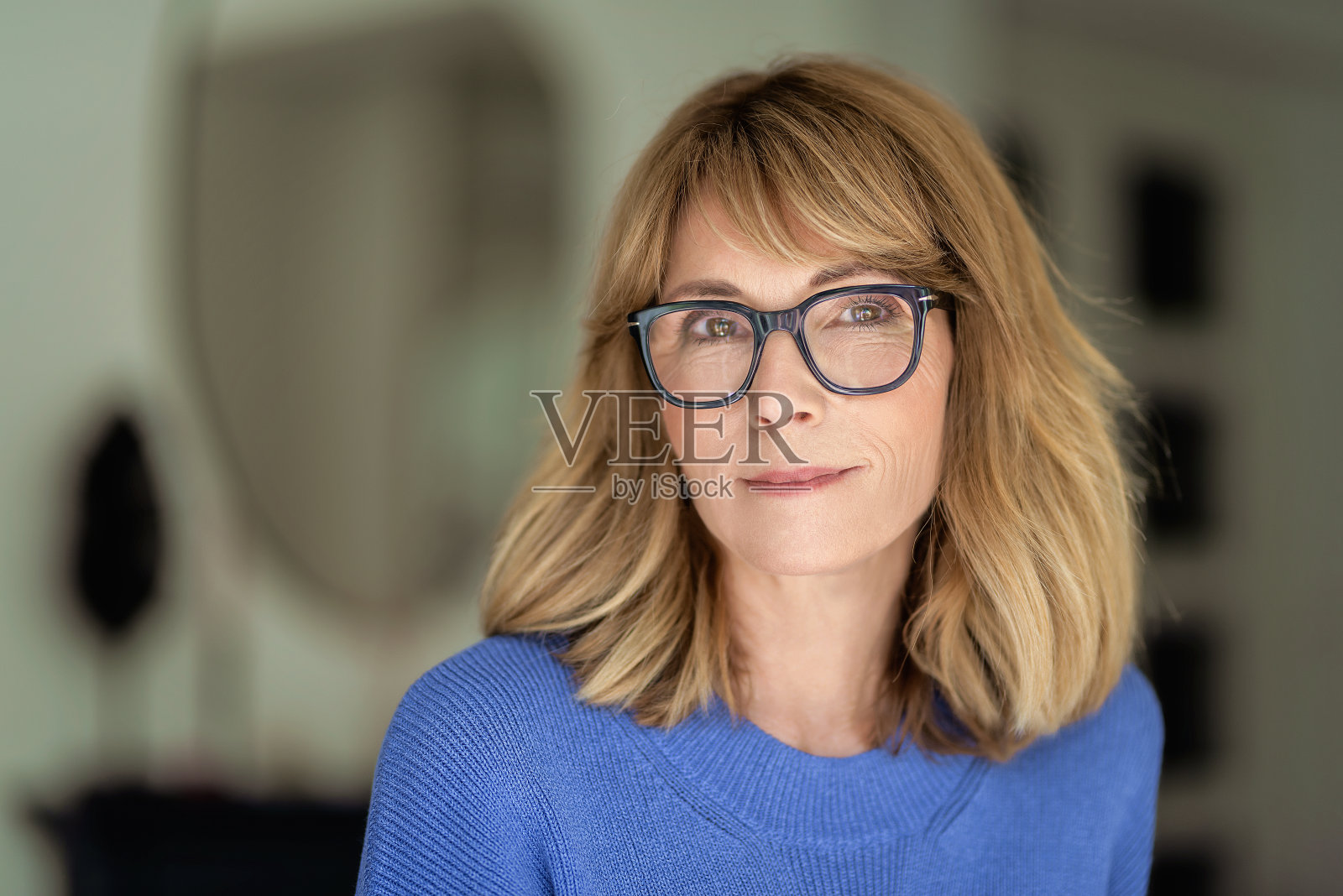 身穿蓝衬衫站在客厅里微笑的金发女人的特写肖像照片摄影图片