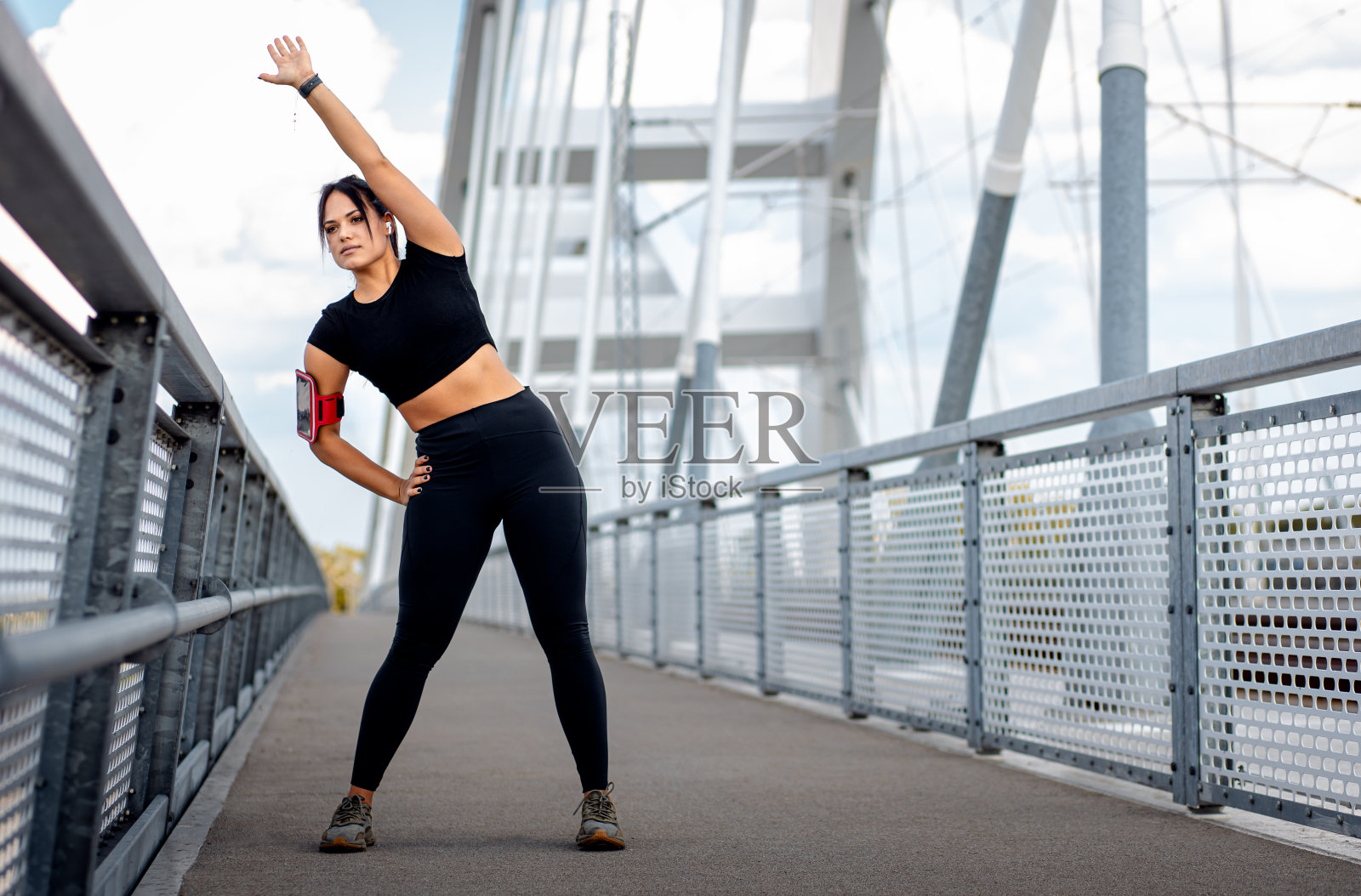 穿着黑色运动服的年轻健身女性准备在桥牌上跑步伸展肌肉。照片摄影图片
