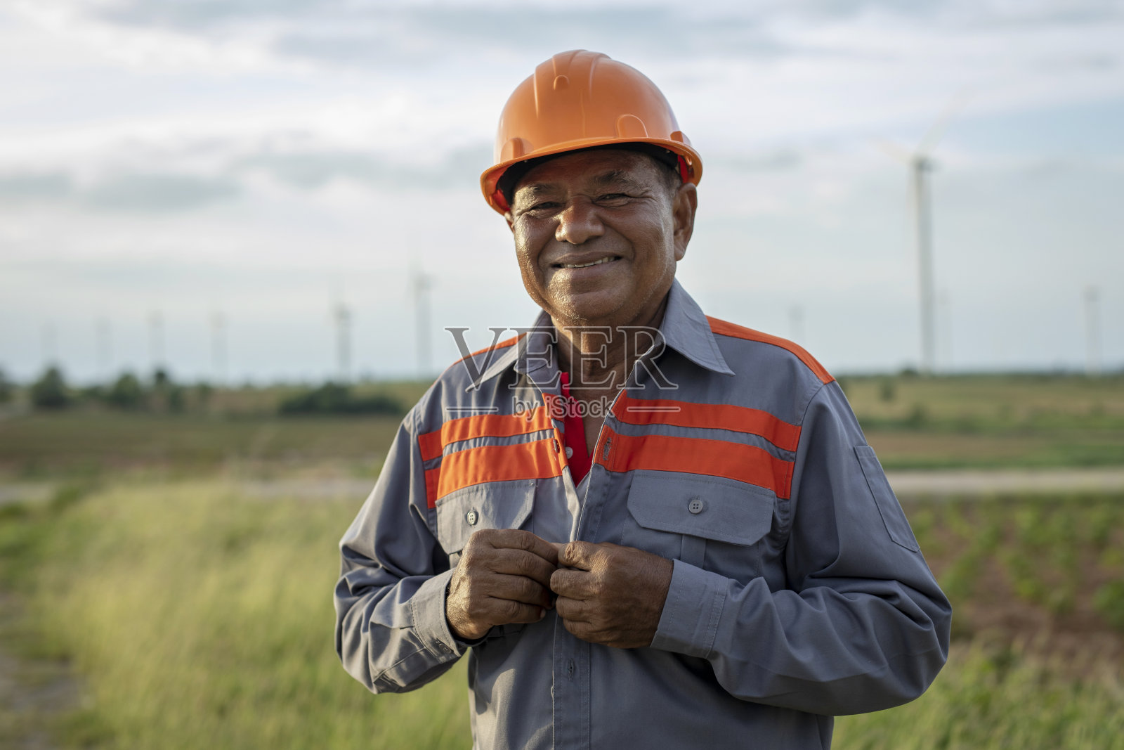 图为一个风电场里,戴着橙色安全帽、面带微笑、快乐的年长男性产业工人看着镜头照片摄影图片