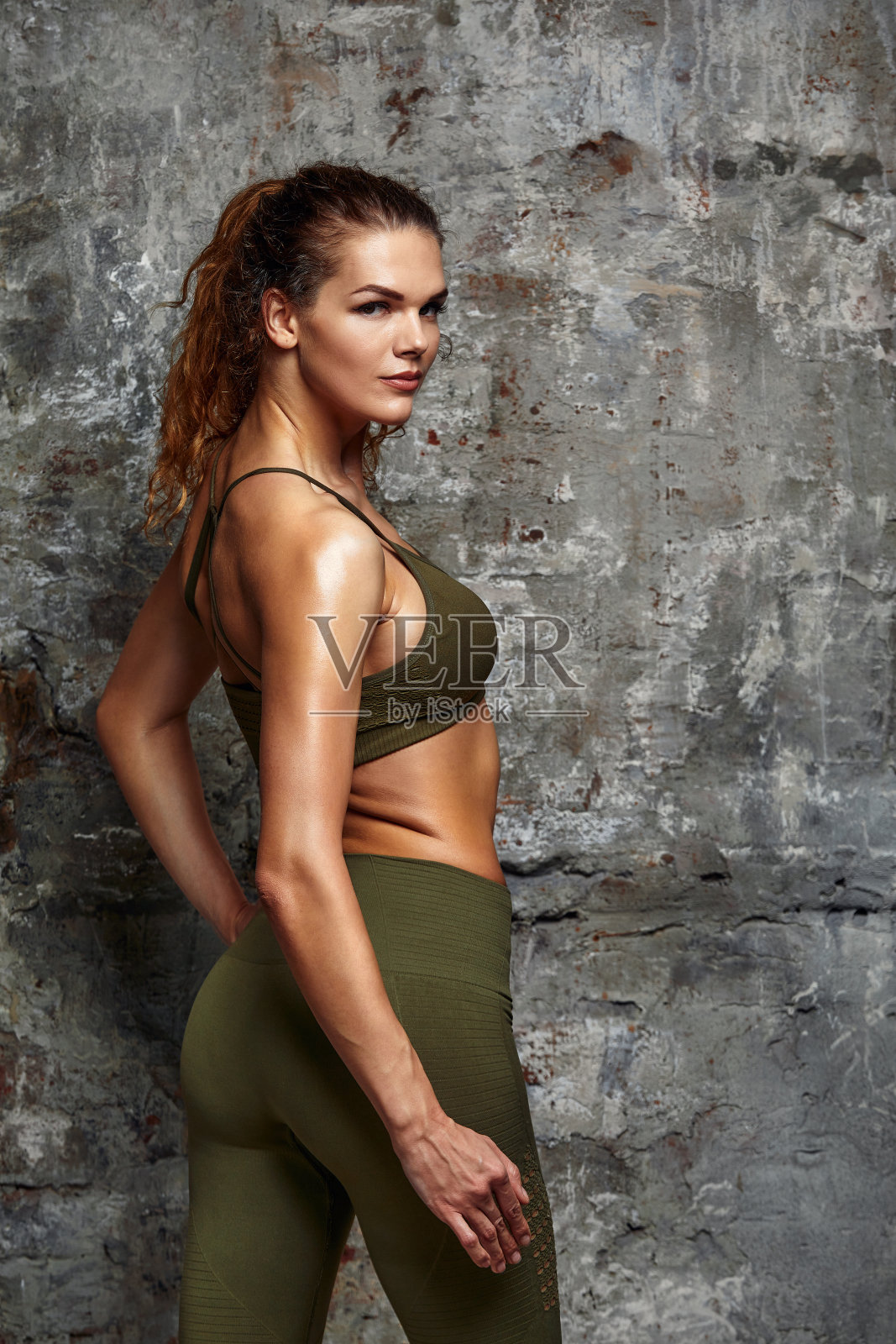 漂亮的运动苗条的女人穿着运动服,腹肌发达,有着积极的生活方式,在灰色的混凝土背景下摆姿势。生活方式的概念照片摄影图片