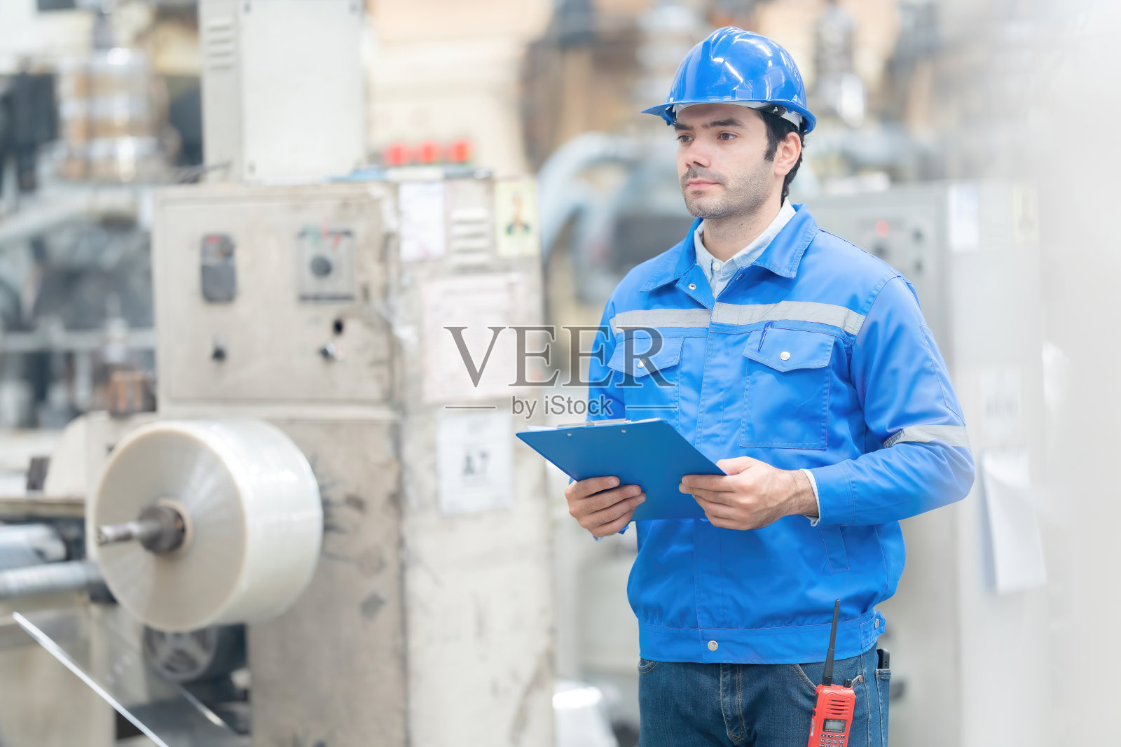 经理是一位从事塑料和钢铁行业的欧洲男性工程师,他拿着笔记本,看着周围运转的机器。戴头盔,穿制服,带上笔记本和收音机。照片摄影图片