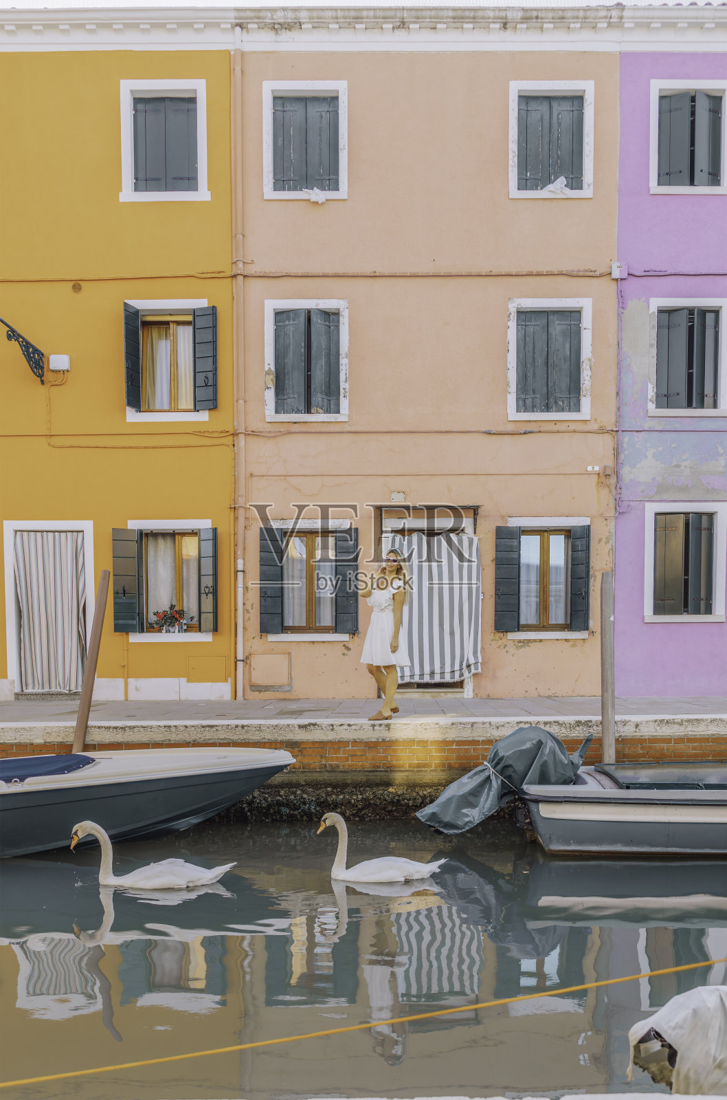 在意大利威尼斯的布拉诺,身着白色夏装的年轻女游客在运河边喂天鹅照片摄影图片