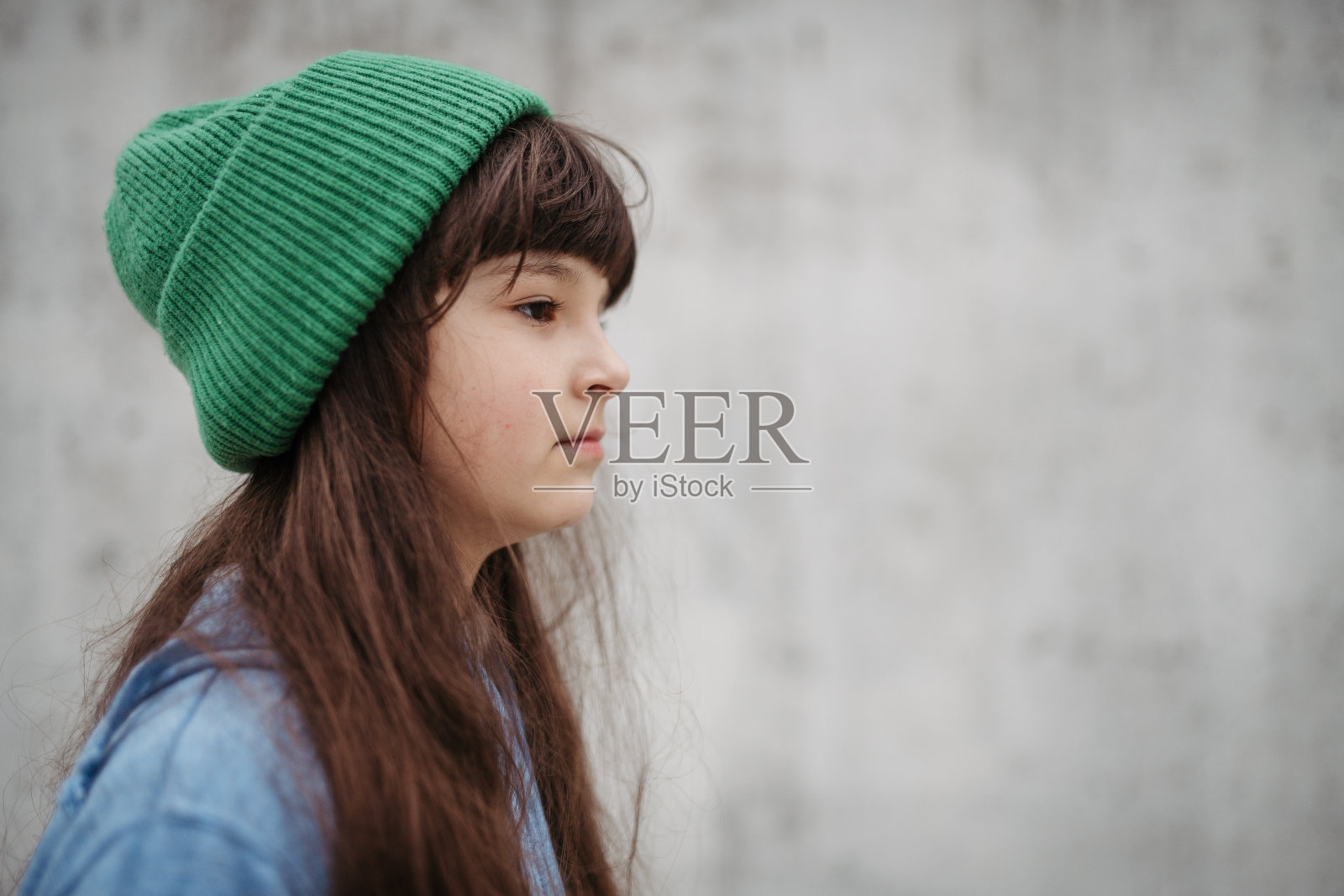 可爱的年轻女孩带着无边帽的侧面肖像。长发女孩站在城市的操场上。照片摄影图片