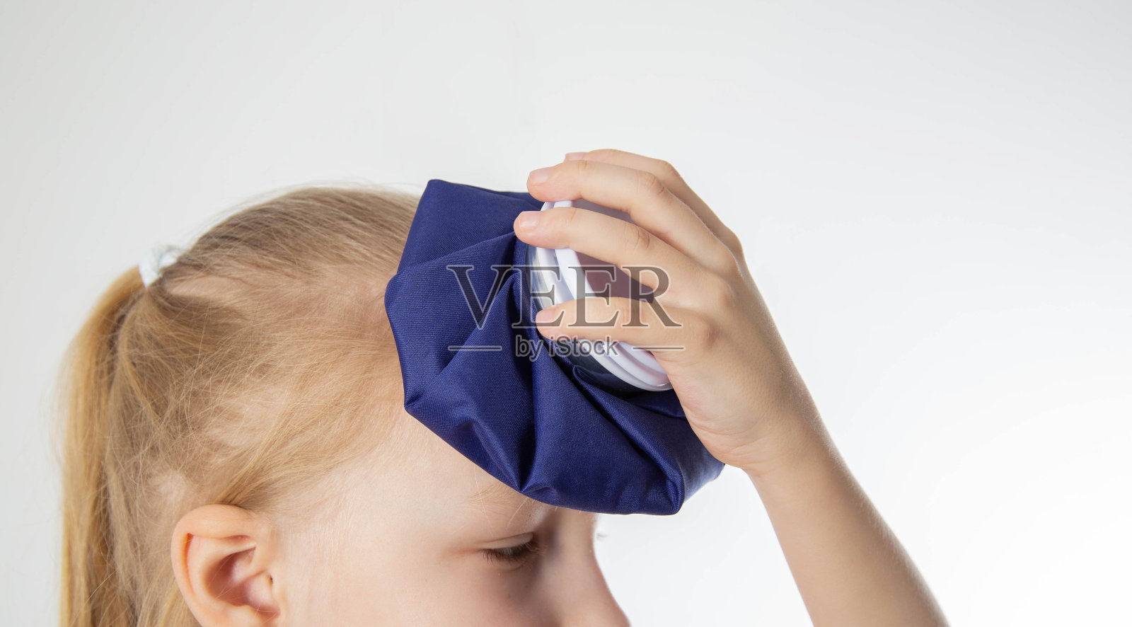 一个小女孩拿着一个冰袋顶在头上。对头部的瘀伤和肿块进行冷敷的概念,特写。当地冷冻疗法照片摄影图片