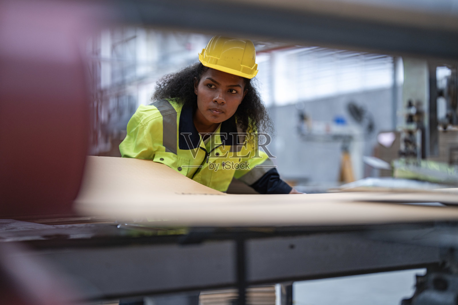 非洲女工的肖像,漂亮的脸,眼睛自信,穿着工作服,戴着安全帽,在工业工厂的重型机器。工程师工人专注于工作场所。照片摄影图片