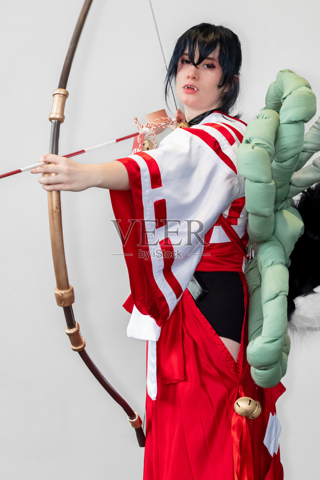 身穿红白相间的服装,脖子上戴着铃铛的女coser手持弓箭摆姿势照片摄影图片