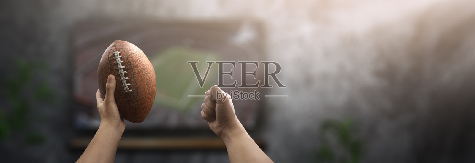 一个兴奋的人拿着球在电视机前看美式足球比赛照片摄影图片