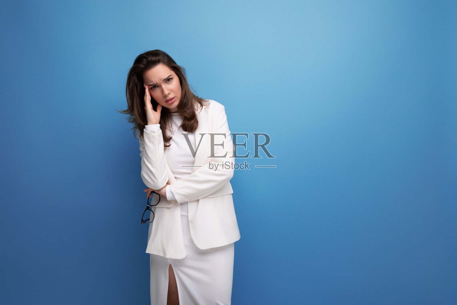 穿着白裙子,戴着眼镜,头痛的年轻女士照片摄影图片