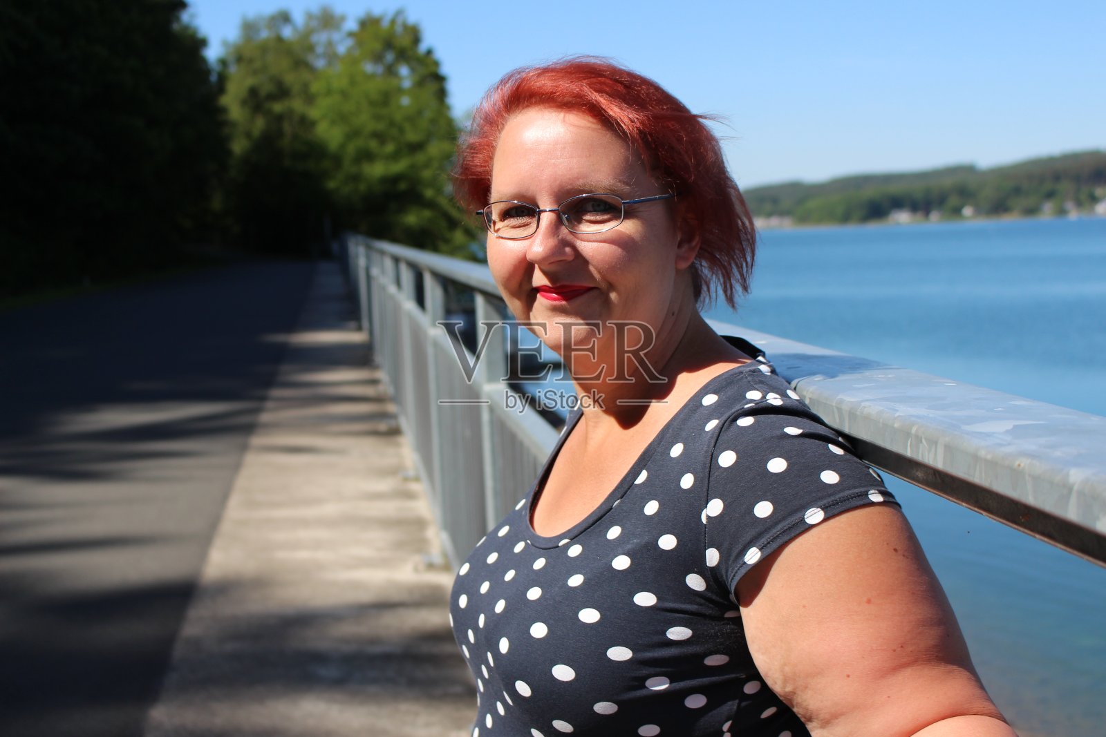 一个戴眼镜、红头发的女人站在湖边照片摄影图片