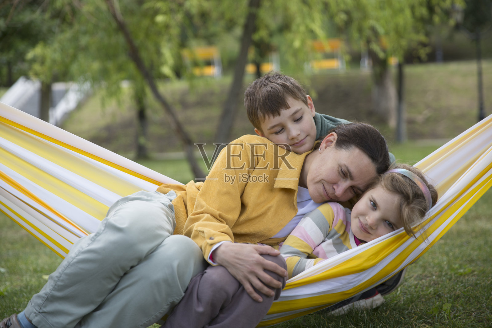 妈妈和两个孩子在夏季公园或花园的吊床上荡秋千。友好家庭的概念。照片摄影图片