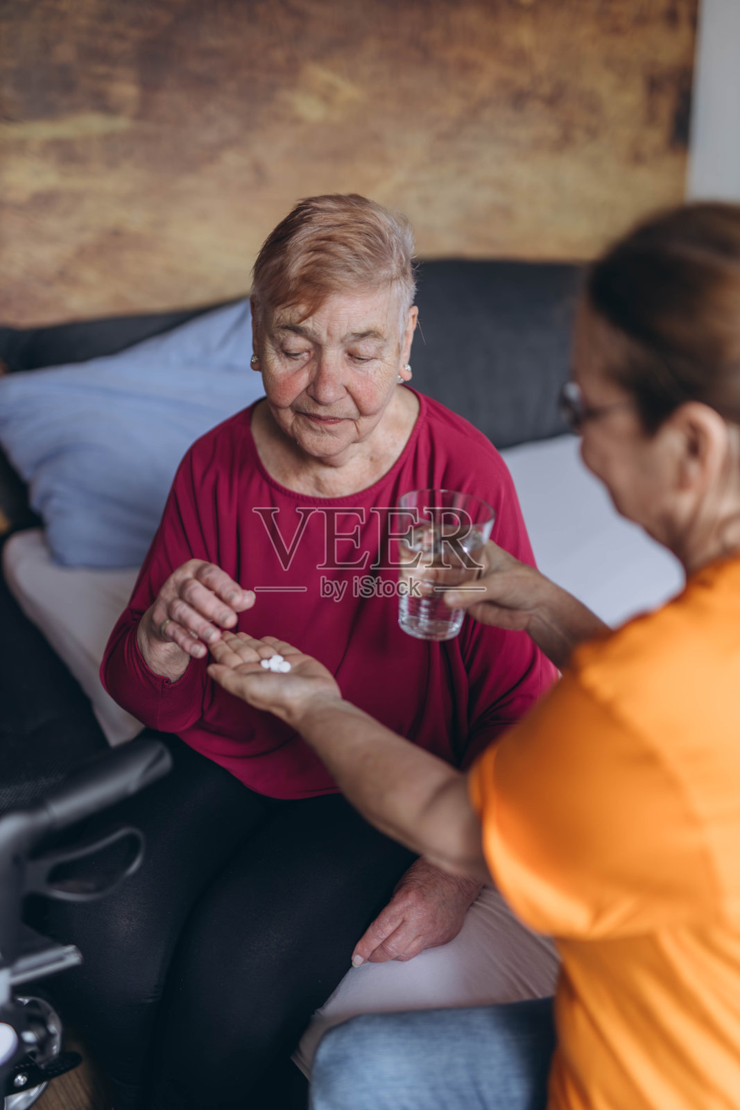 一位老妇人坐在她的床上,一位志愿者给了她一些药片和一杯水照片摄影图片