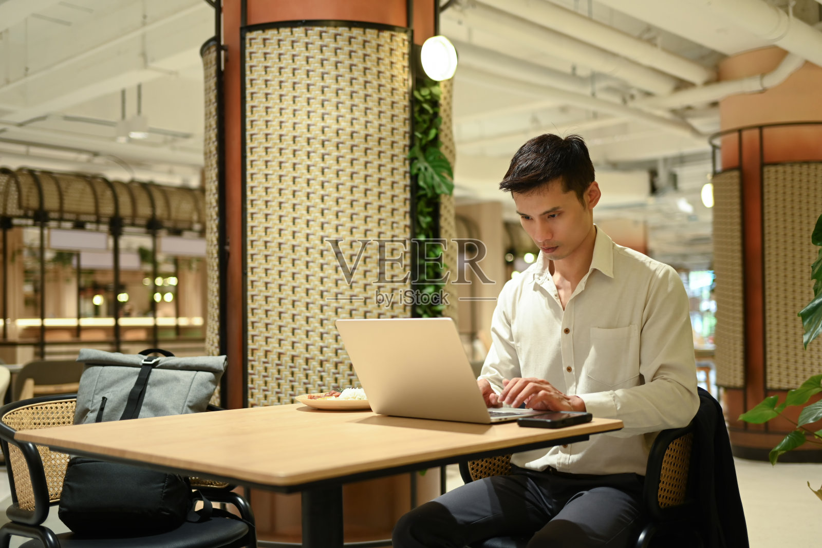 帅气的商人坐在桌子旁,在现代自助餐厅的内部用笔记本电脑工作照片摄影图片