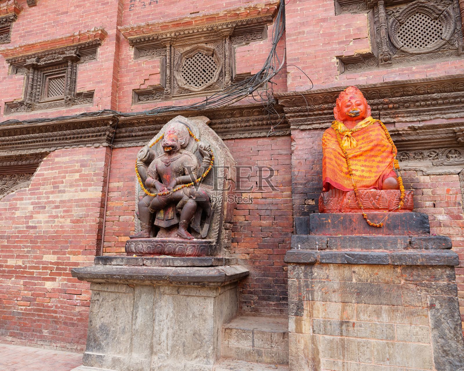 尼泊尔加德满都一堵砖墙前的古代雕像。照片摄影图片