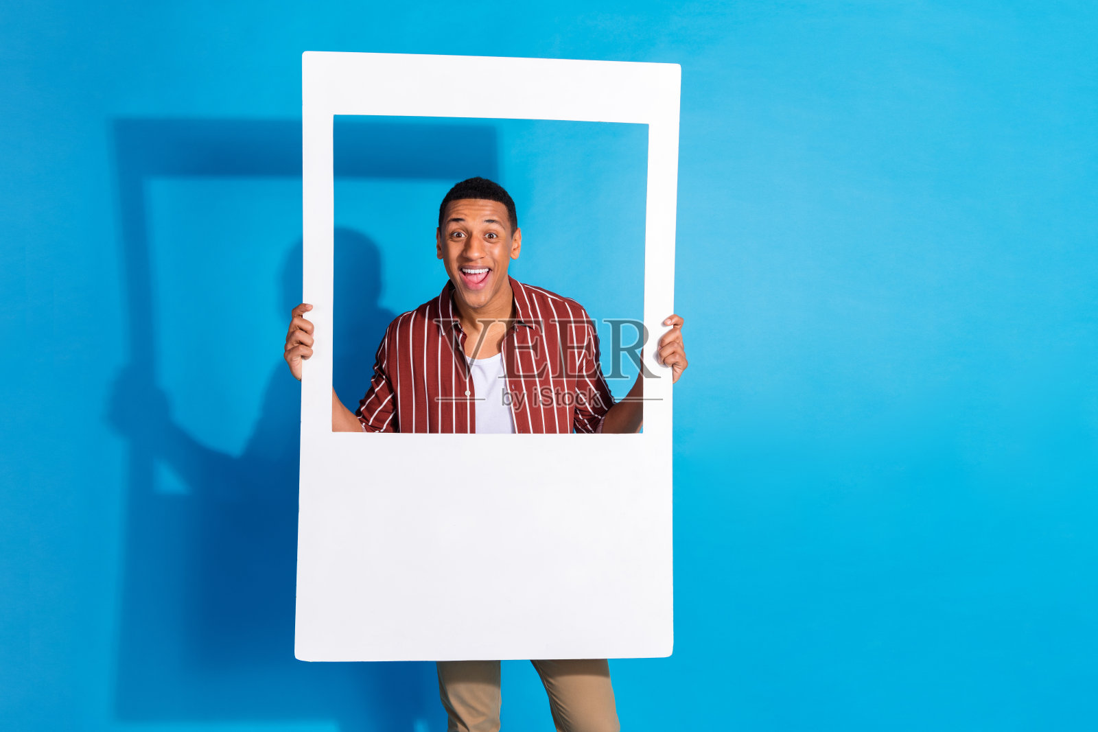 照片喜出望外的好心情的好男人穿条纹时尚衬衫在白色t恤hold相框孤立的蓝色背景照片摄影图片