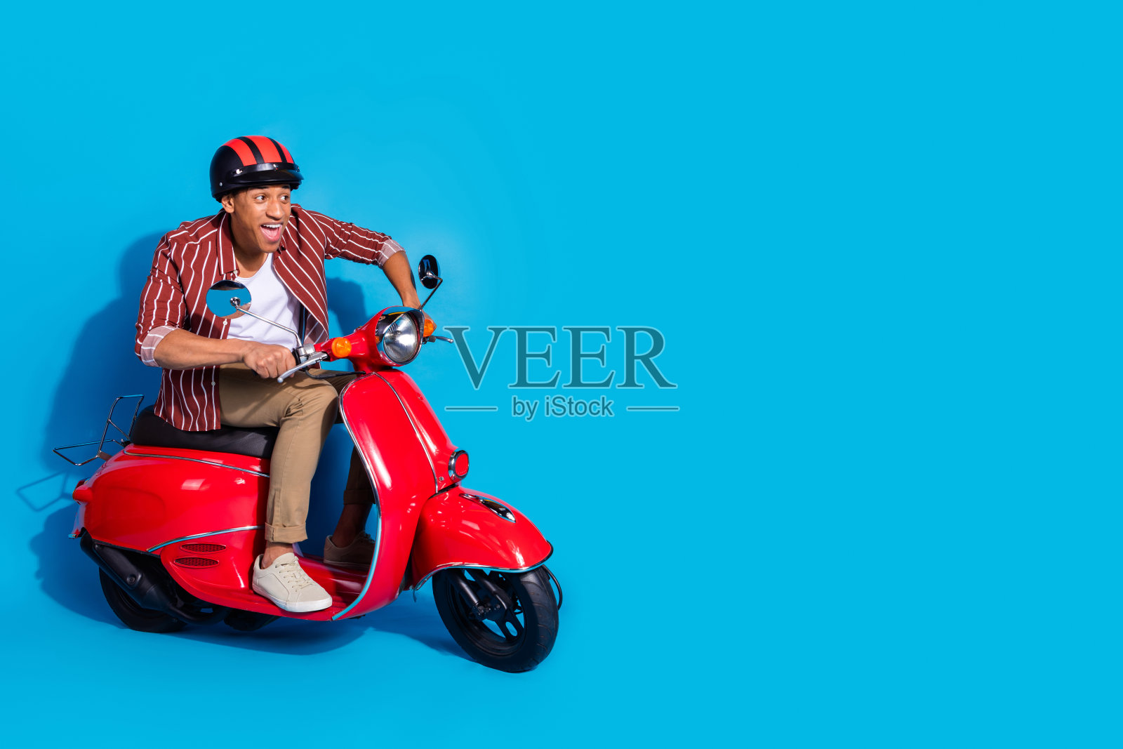 欣喜若狂的家伙穿着时尚的t恤头盔快速骑在助力车上看空旷的空间孤立的蓝色背景的全长照片照片摄影图片