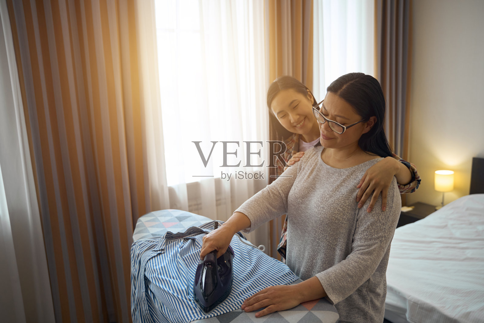 慈爱的父母正在为女儿熨一件皱巴巴的衣服照片摄影图片