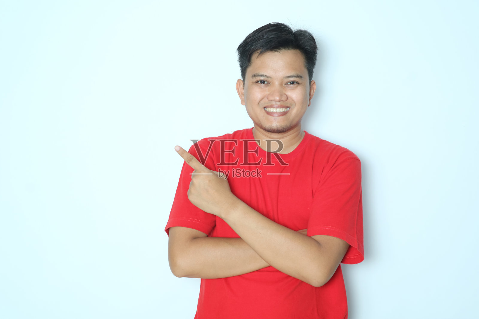 年轻的亚洲男子微笑着用手指向右边。穿红色t恤照片摄影图片