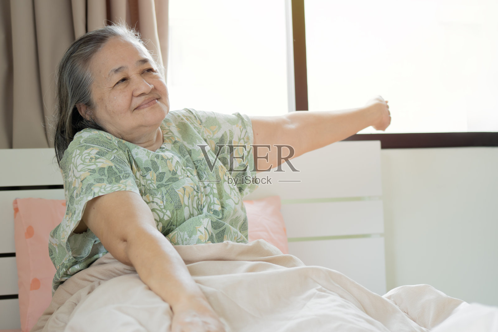 神清气爽的60多岁老年女性早晨醒来,坐在家中明亮卧室的床上舒展身体。照片摄影图片