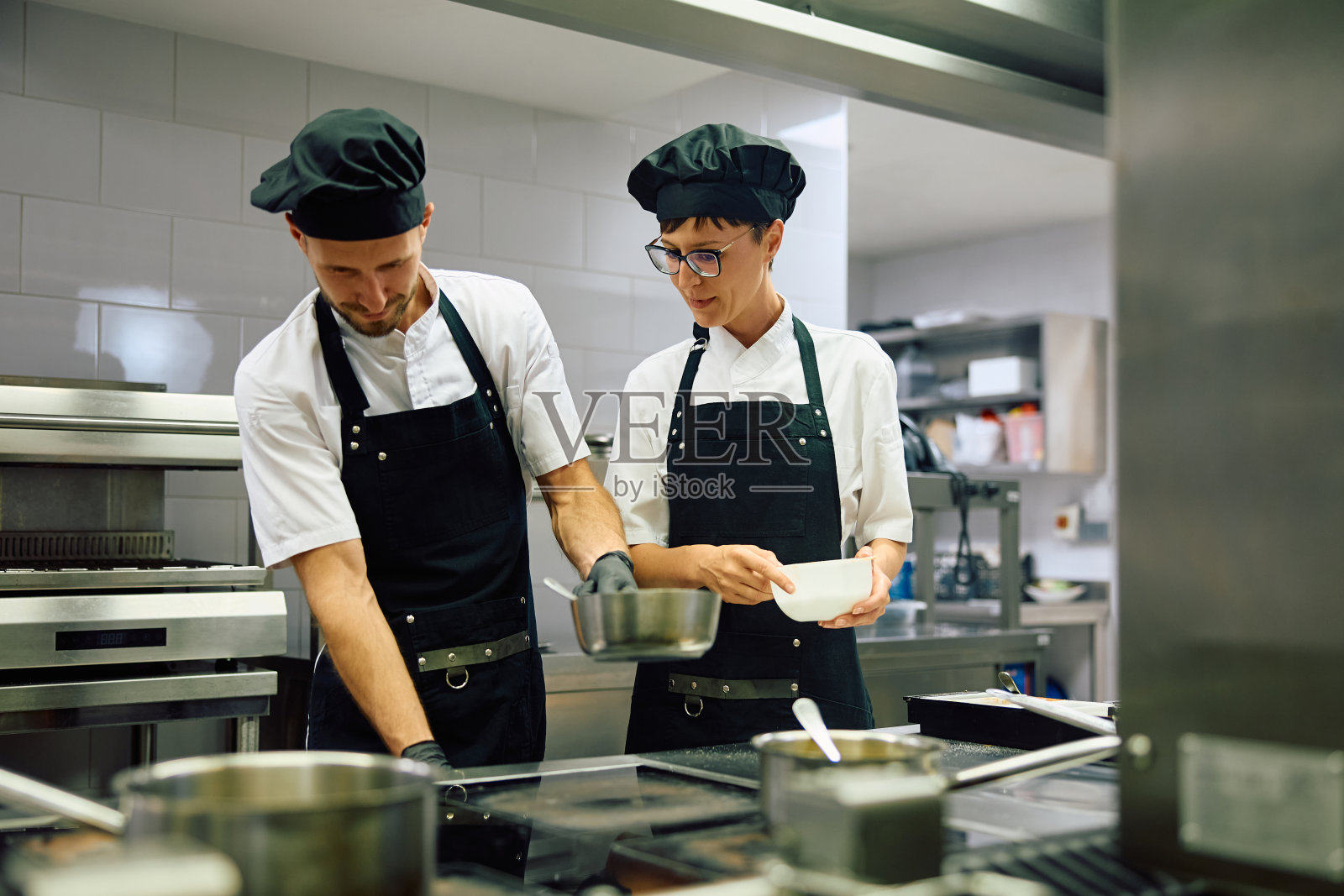 两位厨师在厨房里合作做饭。照片摄影图片
