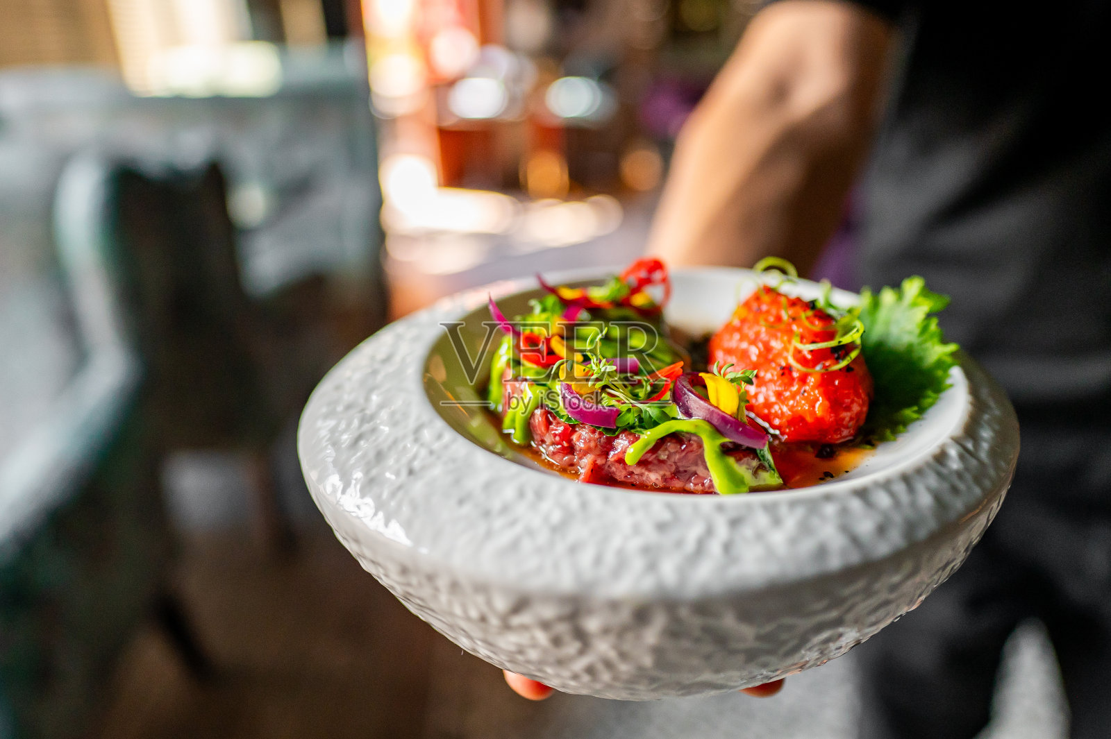 一个人拿着一个白色盘子,盛着红肉,配以绿色香草和紫色洋葱。照片摄影图片