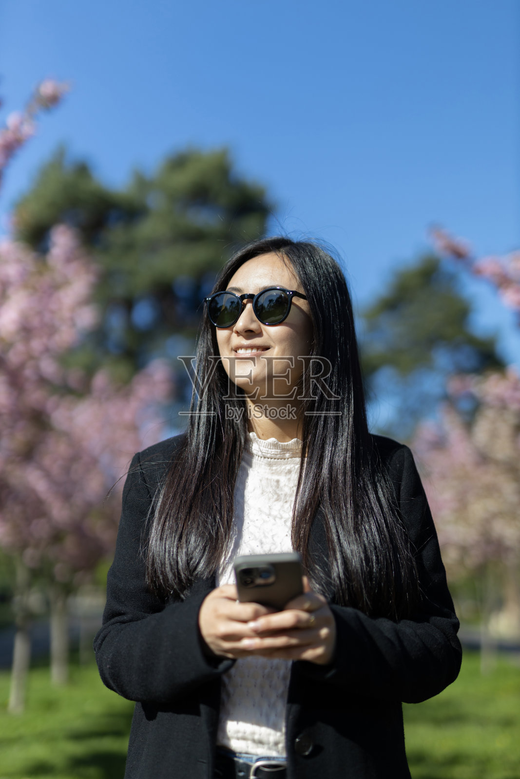 一位亚洲女商人在春天的公园里自信地使用着她的智能手机,享受着快乐的时刻。照片摄影图片