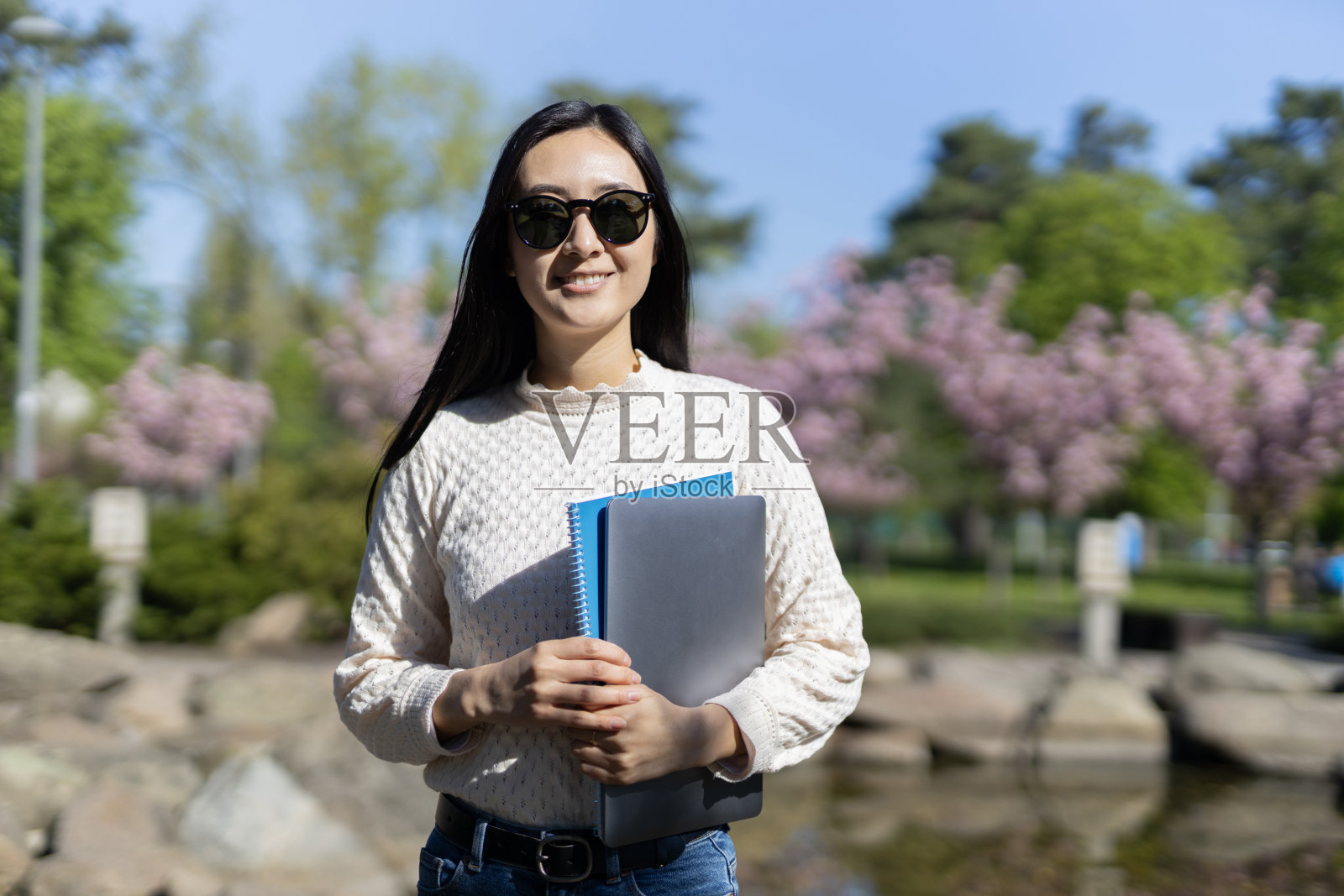 图为,一名亚洲学生在公园外拿着书微笑,展现了教育的乐趣。照片摄影图片