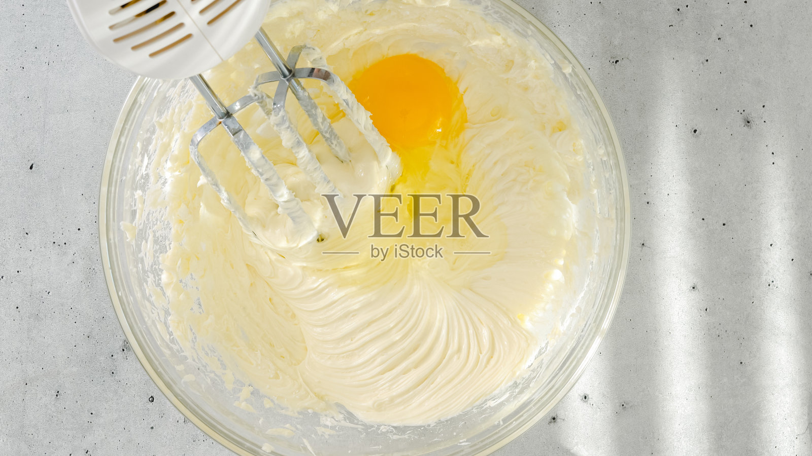 奶油奶酪、鸡蛋和糖放在碗里。芝士蛋糕的配方,在玻璃碗中混合配料,从上方特写照片摄影图片