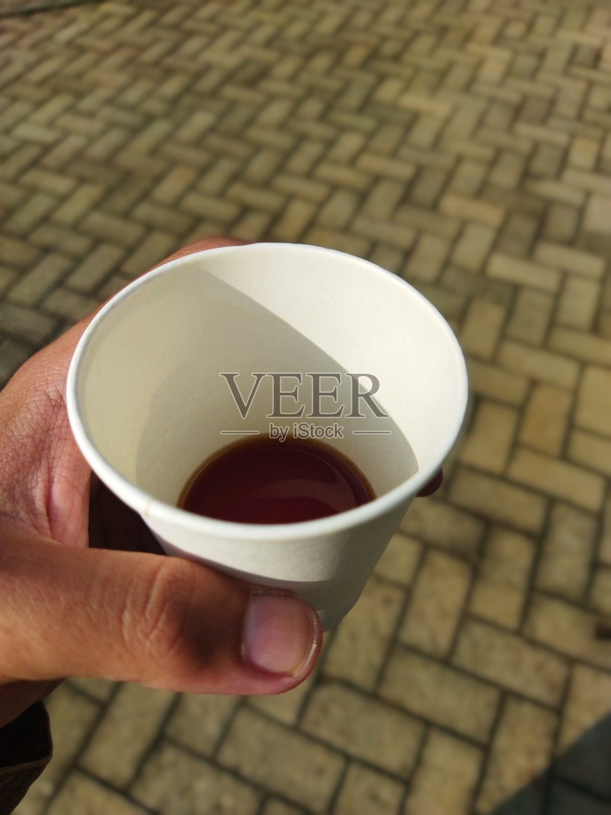 近距离观察手拿着一个装满黑咖啡的纸杯在铺路地板的背景照片摄影图片
