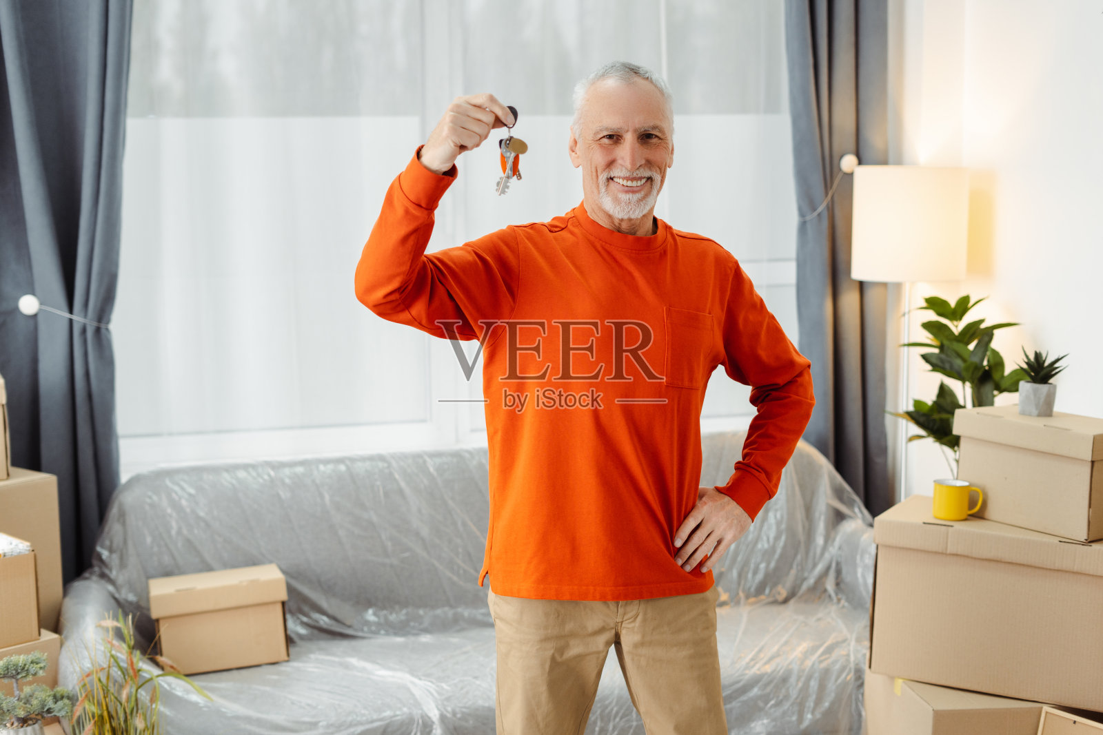 面带微笑的老人拿着新房的钥匙,公寓里堆满了橱柜盒子照片摄影图片