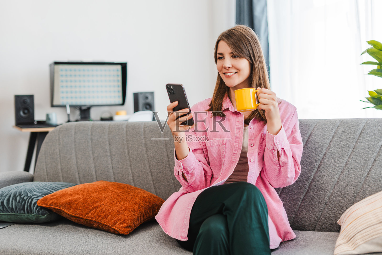 迷人的,微笑的女人坐在家里的床上拿着手机,使用移动应用程序的画像照片摄影图片