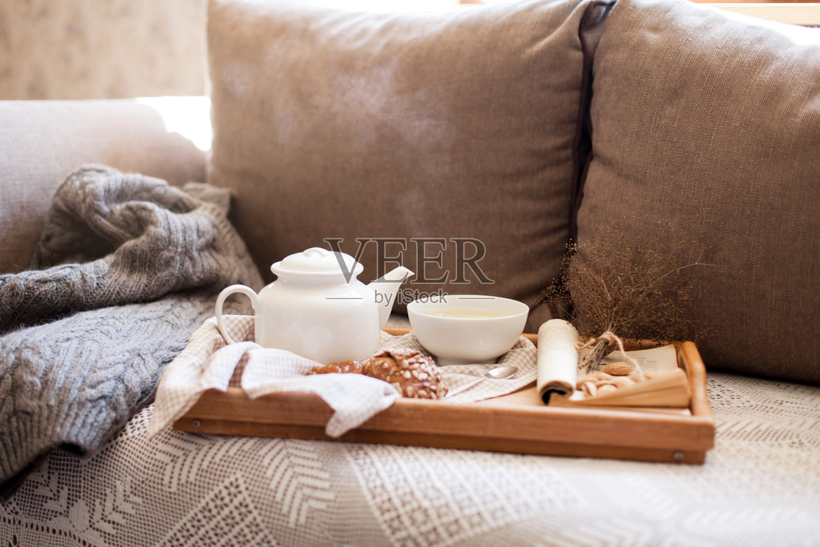 茶壶静物,一杯蒸汽热茶在温馨的家居室内。食物、饮料、书都放在木制托盘上照片摄影图片