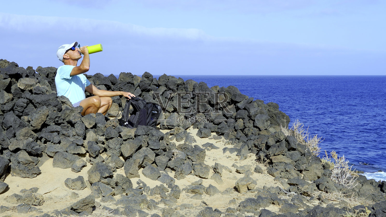 露营者在面朝大海的石头帐篷里用铝瓶喝水照片摄影图片