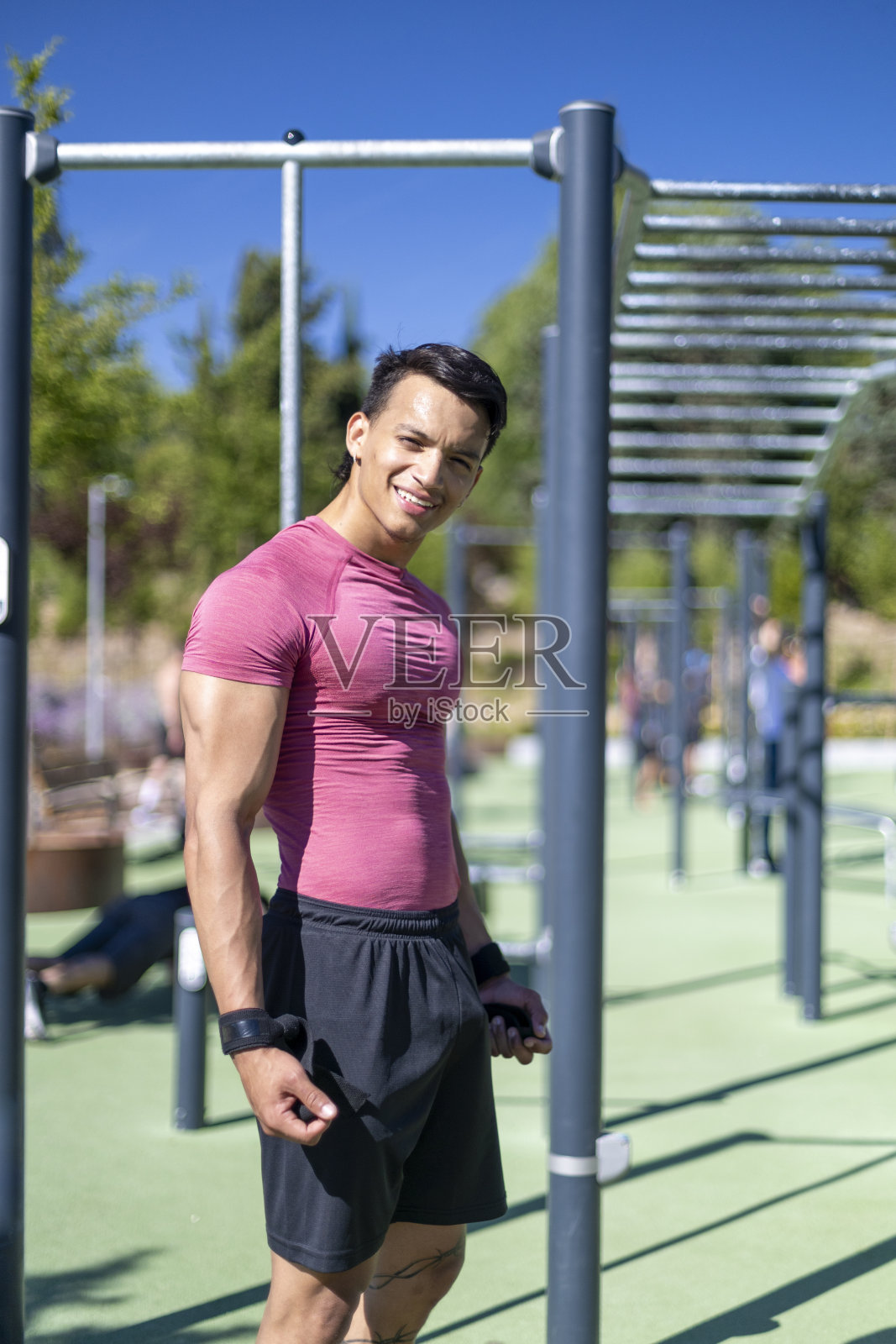 在一个阳光明媚的日子里,穿着粉色衬衫的拉丁裔男子微笑着站在户外健身操公园。照片摄影图片