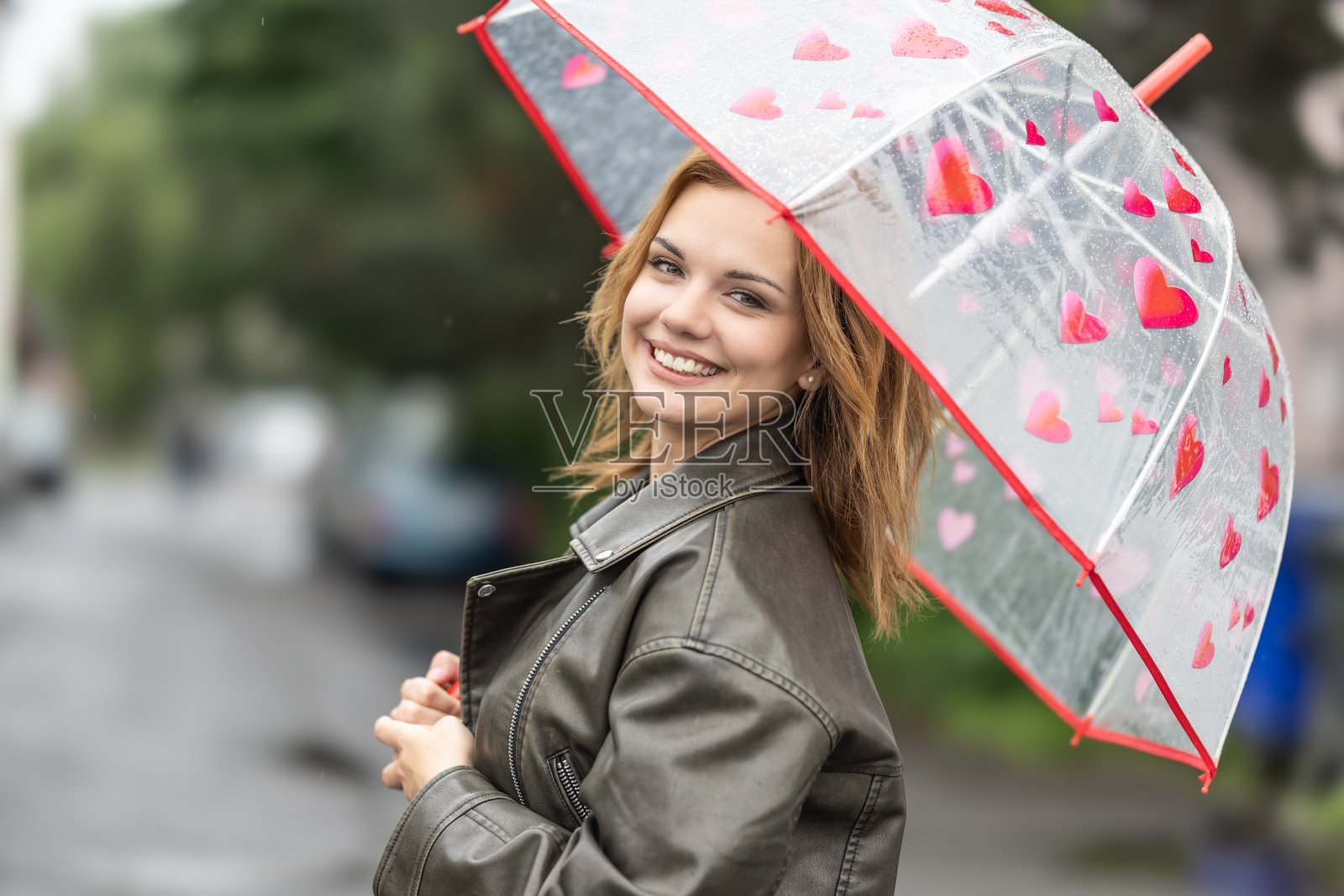 一个年轻的微笑的女人在伞下,心情很好,尽管下雨。照片摄影图片