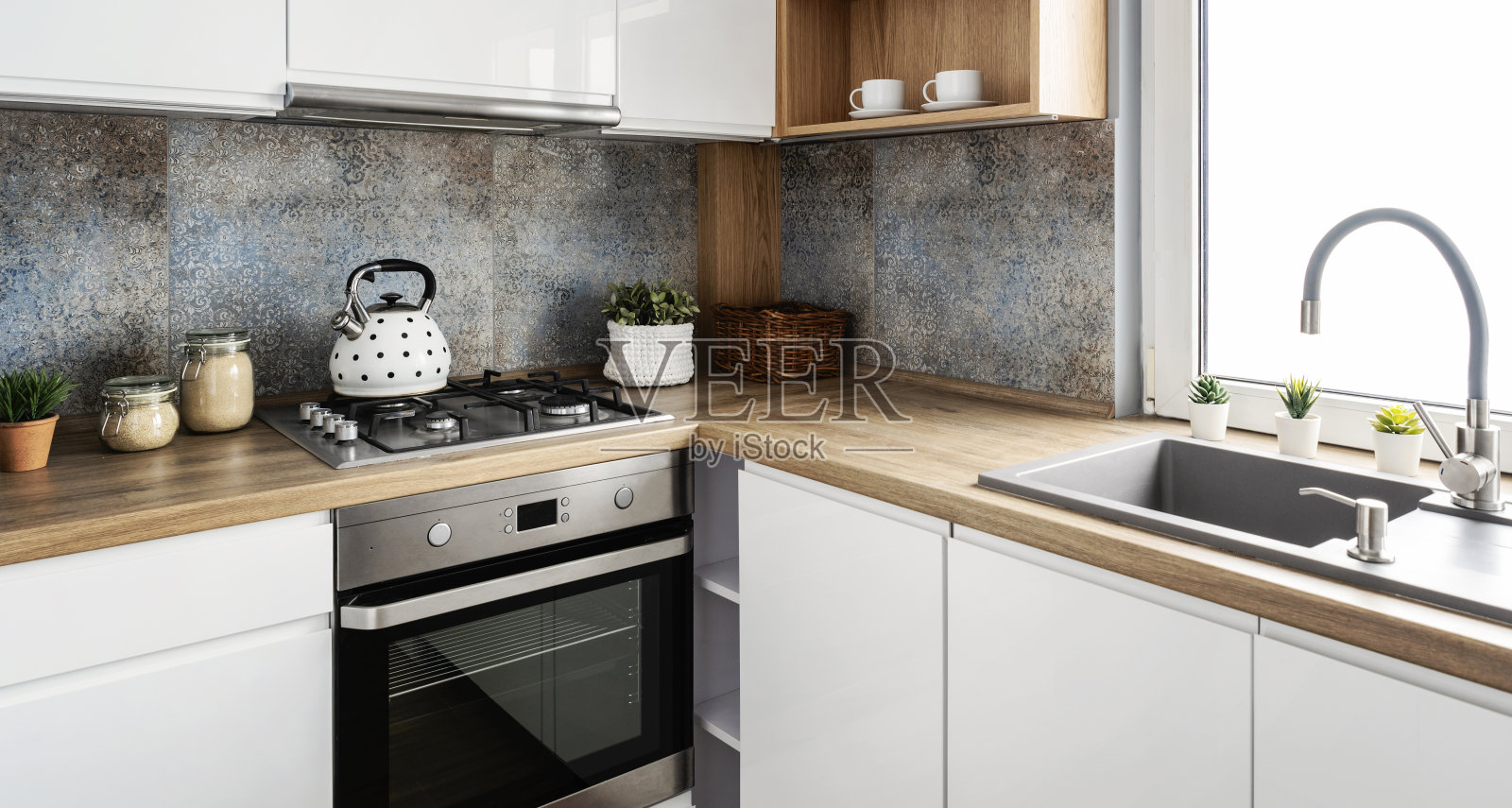明亮的室内现代厨房,木质台面,带水壶的玻璃陶瓷灶台和墙上的图案瓷砖。家居装饰。照片摄影图片